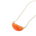 Carnelian gemstone charm carved like an Ojai Pixie tangerine slice with 14k gold ring, hanging from a gold chain on a vintage green book.