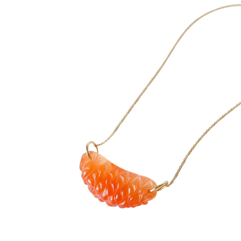 Carnelian gemstone charm carved like an Ojai Pixie tangerine slice with 14k gold ring, hanging from a gold chain on a vintage green book.